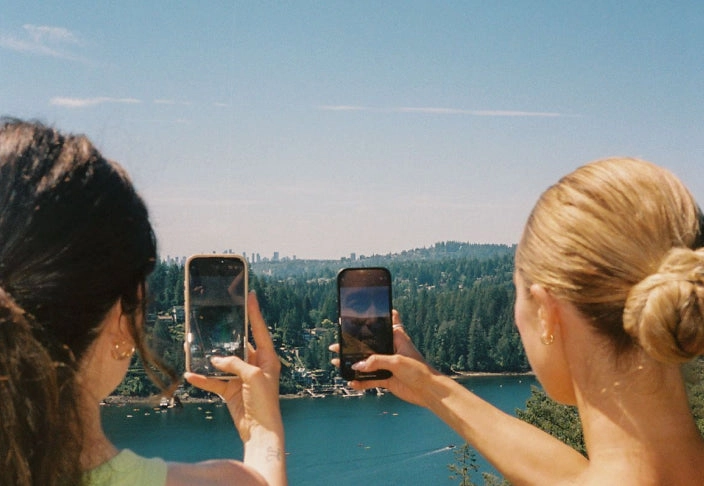 Two women photographing a lake with their phones