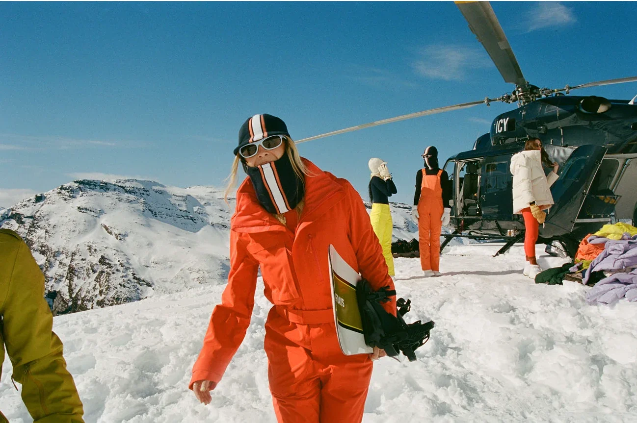 Skier in an orange suit walking away from a helicopter on snow