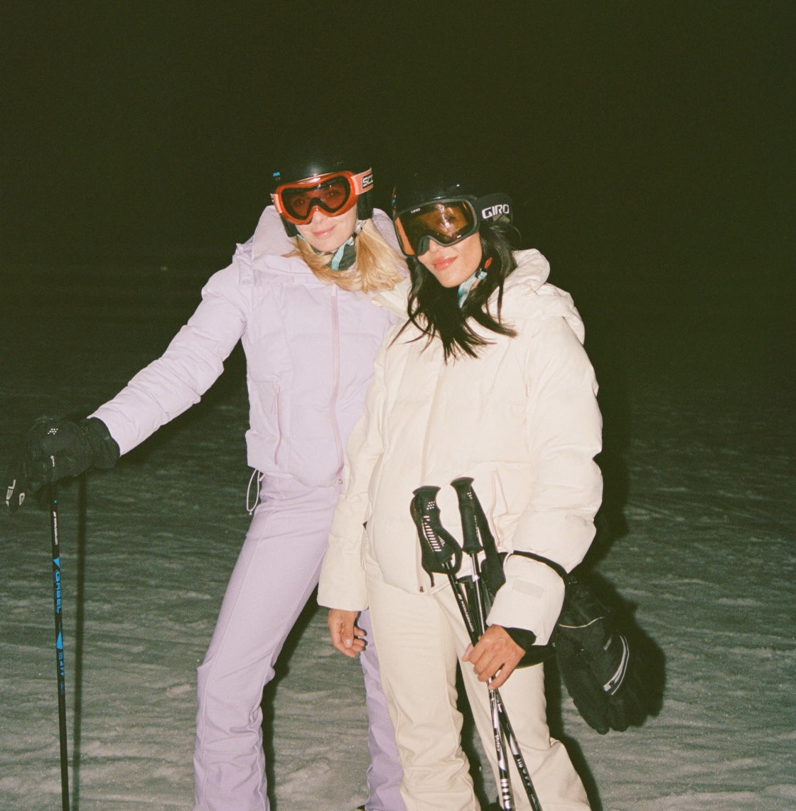 Two skiers in white and lavender gear at night holding poles