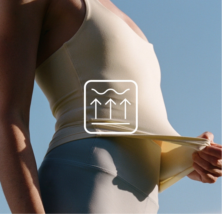 Close view of a cream tank top with a hand tugging at the hem