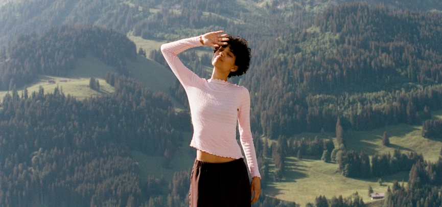 Woman in a light pink top on a green mountainside
