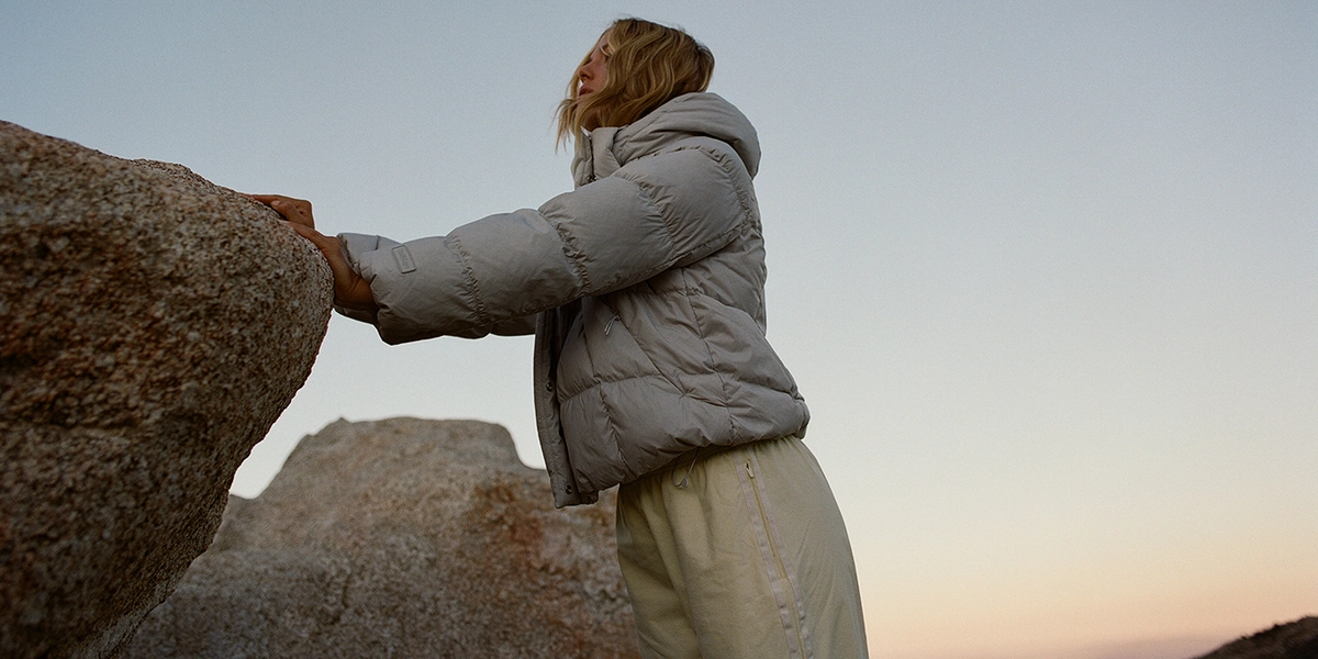 Person in a gray puffer jacket climbing a boulder at sunset